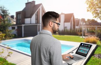 A man with laptop by a swimming using a pool automation system.