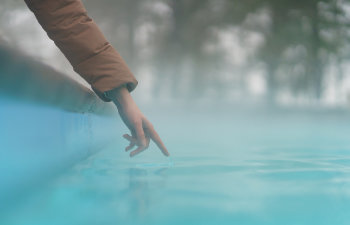 hand of woman checking temperature of water in open swimming pool in winter